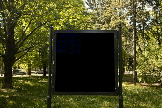 Mockup of the blank street city outdoor advertising square billboard in black frame at park entrance photo