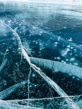 Texture of beautiful blue ice with cracks and air bubbles in the frozen lake photo