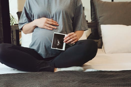 Cropped shot of pregnant woman holding pregnancy ultrasound or baby sonogram while sitting on bed photo