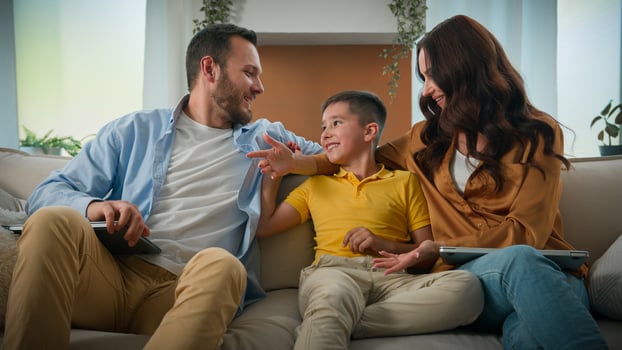 Man woman parents freelancer working remote at home on couch using laptop kid boy child distract mom and dad from work loving caring mother father finish typing happy Caucasian family hugging embrace photo