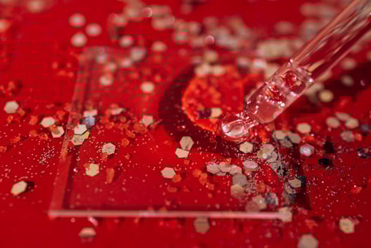 Transparent serum or oil glass bottle with pipette. Bright red background with silver glitters and confetti photo