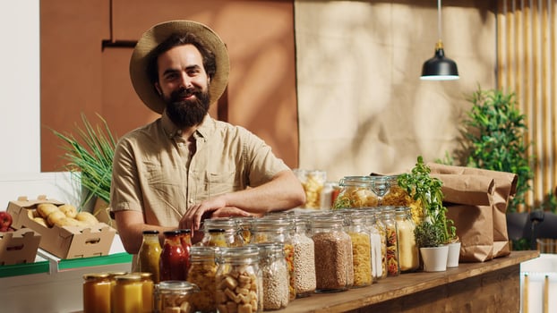 Portrait of smiling vegan man in eco friendly zero waste supermarket using shopping basket to purchase bulk items in ecological containers. Client in local bio grocery shop buying additives free food photo