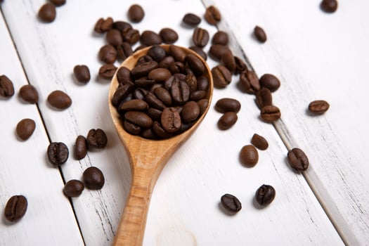 roasted coffee beans with wooden spoon on a white wooden background close up photo