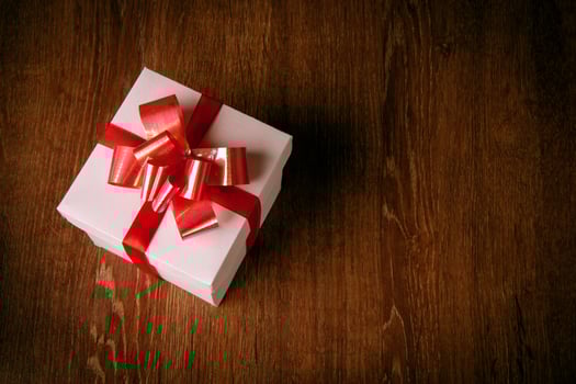 One white festive gift box with a red bow on a wooden table photo