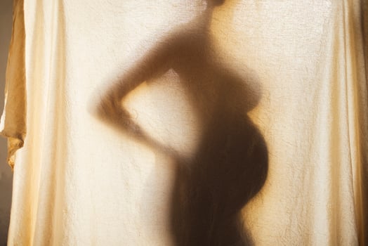 Shadow silhouette of a female pregnant behind a textured fabric. photo