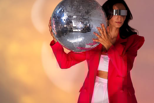 A young fashionable woman in a pink jacket holds a large sparkling disco ball photo