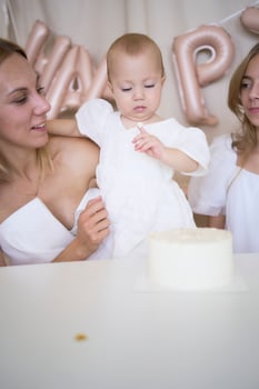 baby girl tries her first birthday cake with mom and pre-teen sister photo