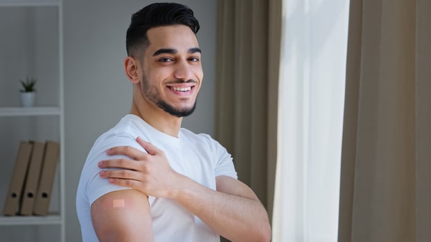Happy satisfied indian guy arab man hispanic patient male posing indoors wears white t-shirt shows plaster on shoulder feels relief after vaccination injection with covid remedy medical immunization photo