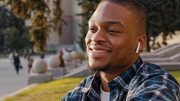 African american handsome young man listening music wireless headphones in city town center. Close up portrait multiracial guy student enjoying song audio sound with earphones smiling outdoors photo