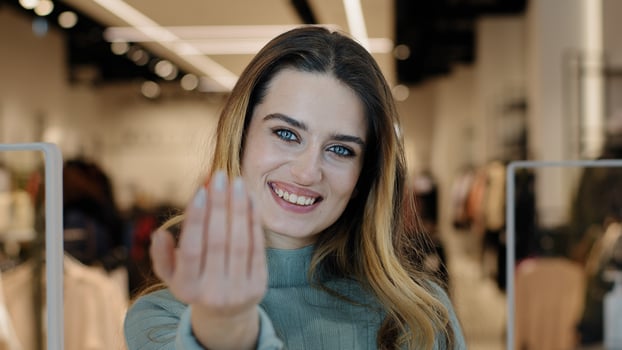 Portrait caucasian female shopper seductive smiling woman saleswoman owner of clothing store looking at camera making gesture hey you come here inviting waving hand offer discount tempting approaching photo