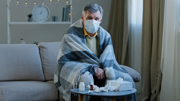Upset sick grandpa in medical mask sitting on couch caucasian elderly man wrapped in blanket feel chills ill mature senior looking at camera symptoms covid 19 epidemic coronavirus outbreak flu concept photo