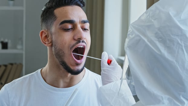 Unrecognizable nurse medical worker doing pcr test with equipment for covid-19 coronavirus to ethnic guy. Close-up spanish man arabic male patient opens mouth donates saliva sample for infection virus photo