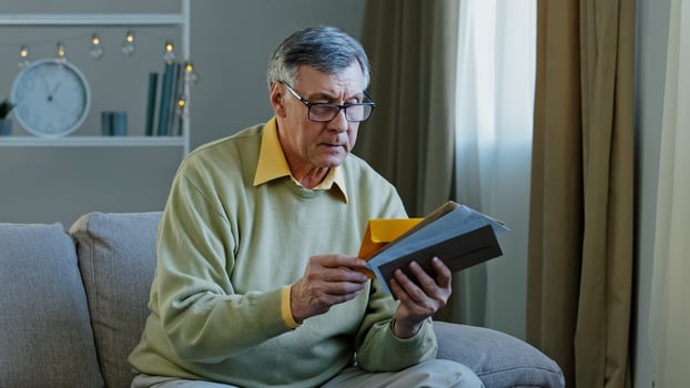 Old 60s elderly Caucasian man checking sorting letters in living room concentrated mature grandfather sitting on sofa looking at correspondence notice bank account aged pensioner check bills postal photo