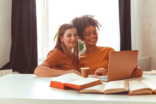 Two happy girlfriends sitting in front of laptop computer, preparing for exams together at home photo