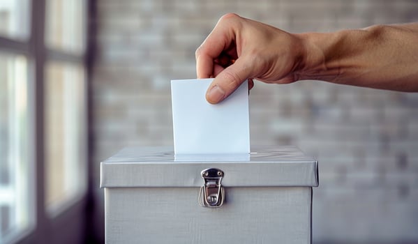 A person is putting a white piece of paper into a box. The box is silver and has a lock photo
