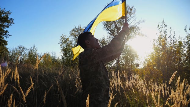 Male military in uniform waving flag of Ukraine at countryside. Young soldier of ukrainian army lifting blue-yellow banner as symbol of victory against russian aggression. Invasion resistance concept. photo