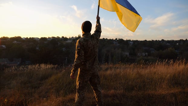 Male soldier stands with raised flag of Ukraine against background of beautiful sunset. Male ukrainian army soldier with a lifted blue-yellow banner in honor of the victory against russian aggression photo