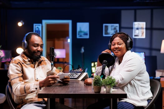 Black journalist uses modern recording technology to interview smiling female content creator in home studio. They broadcast their lively conversation to online audience via social media platforms. photo