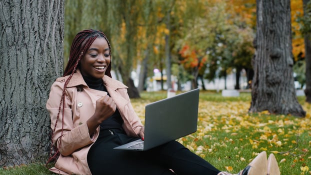 Excited african american woman sitting in autumn park playing online game on laptop gambling competition happy young girl winner celebrating victory enjoying success winning lottery using computer app photo