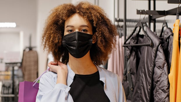 African american girl shopper consumer buyer curly woman client wears medical protective mask walks from clothing boutique store with shopping bag package purchase buy sale discount covid quarantine photo