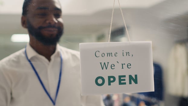 African american man working in clothing store opening in the morning, waiting for customers. Happy BIPOC retail clerk turning closed message sign on fashion boutique door in mall photo
