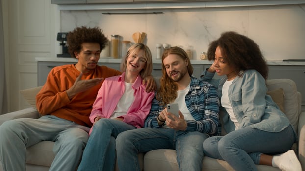 Multiracial people multiethnic friends diversity students Caucasian women female girls African American men male guys together home couch sofa looking at mobile phone discuss talking news social media photo