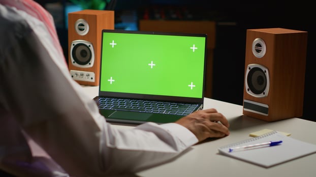 Muslim man scrolling on green screen laptop while working from home. Self employed man sending emails from chroma key device in apartment office with TV as background noise photo