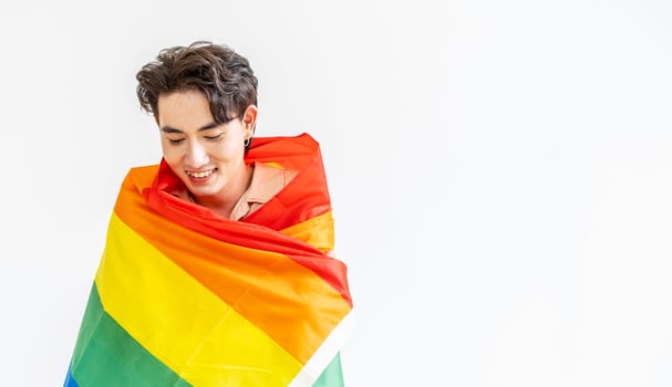 Portrait of transgender or gay man smiling in front of camera taking cover with lgbt flag on white background with copy space. People lifestyle fashion lgbtq concept photo