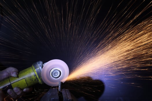 a close up of a hand holding an angle grinder to polish a pice of metal.sparkls fly from the point of contact.the worker is holding the grinder with one hand photo