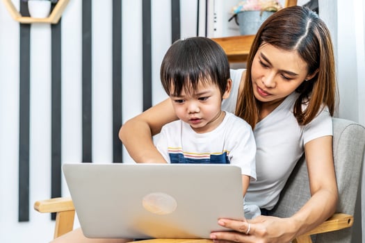 Young asian mother her little adorable son using laptop looking at computer screen enjoying watching funny social media doing online shopping relaxing on sofa at home together photo