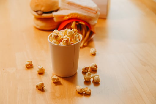 A bucket of popcorn, top-view, warm colors, light brown wooden background, flat lay, daylight macro close-up photo