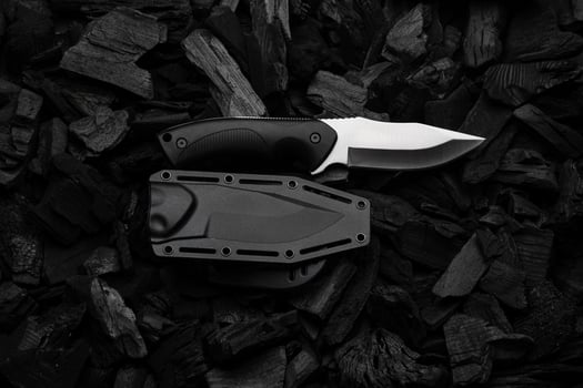 A modern knife with a silver blade and a rubberized handle. Plastic scabbard. Dark charcoal back. photo