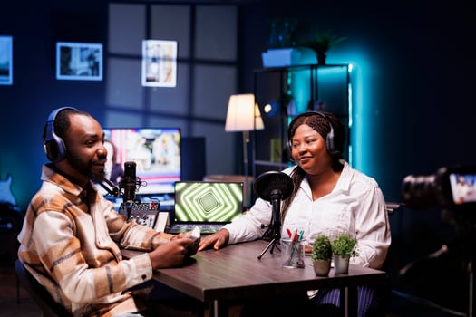 Cheerful media stars recording a podcast in home studio with professional filming equipment for broadcast on live streaming platform. Blogger interviewing celebrity, filming the encounter with camera. photo