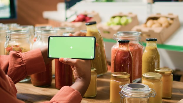 Young woman shops with greenscreen display on smartphone, choosing organic products sold in bulk from local grocery store. Vegan customer searching for locally grown eco friendly produce. photo