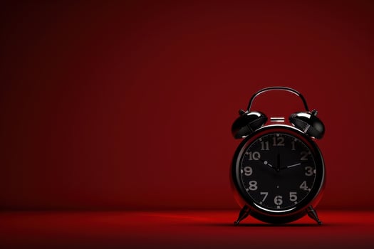 A vintage black alarm clock stands out against a striking red backdrop, capturing the essence of time on a quiet afternoon photo