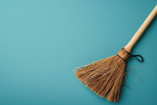 A rustic broom rests on a vibrant teal surface, ready for cleaning tasks with its natural bristles catching the light photo