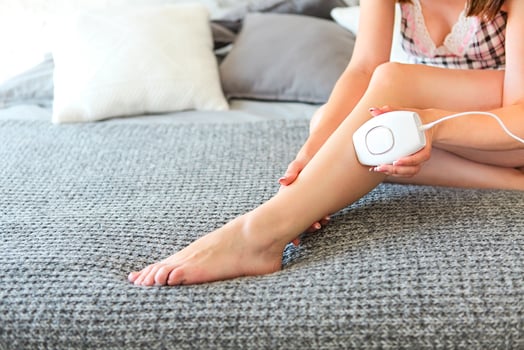 Young brunette woman holding a appliance for photo-epilation sitting on the bed photo