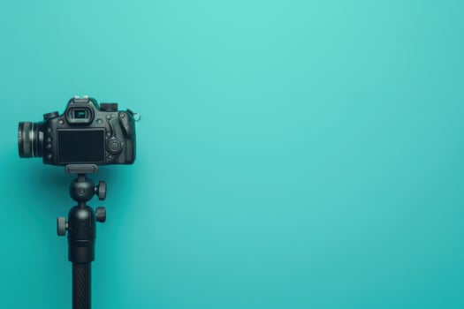 A black camera on a tripod against a vibrant turquoise background, ready for photography in a creative workspace photo