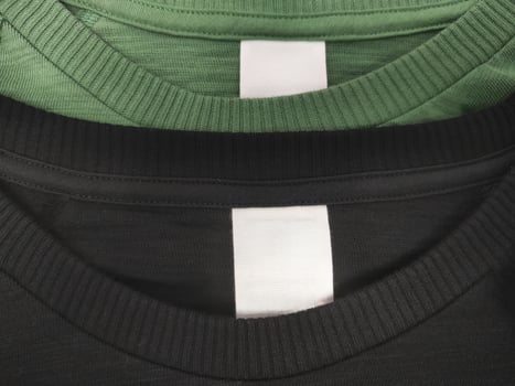 Two cotton T-shirts black and green with a blank white label indicating the size of the clothes and washing instructions photo