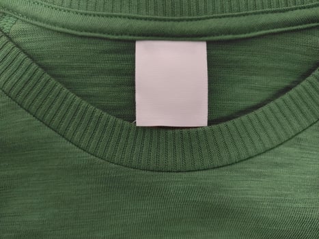 Blank white label indicating clothing size and washing instructions on green background of cotton t-shirt photo