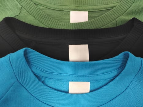 Three T-shirts black blue and green with Blank white label indicating clothing size and washing instructions photo