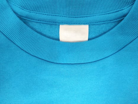Blank white label for clothing size and washing on blue background of t-shirt fabric texture photo