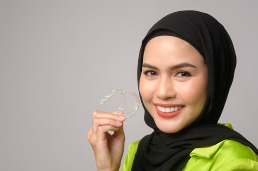 Muslim woman with hijab holding invisalign braces in studio photo