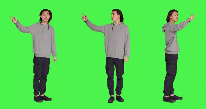 Model showing left or right directions in studio, pointing to both sides and indicating another path. Asian young adult advising someone to go that way, full body greenscreen backdrop. photo