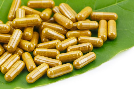 Turmeric Powder in Transparency Hard Gelatin Capsules with Green Natural Leaves on White Background. photo
