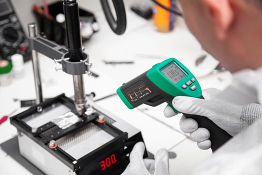 The master measures the temperature of the microchip at the soldering station with a laser thermometer. Service center. Repair of microelectronics. photo