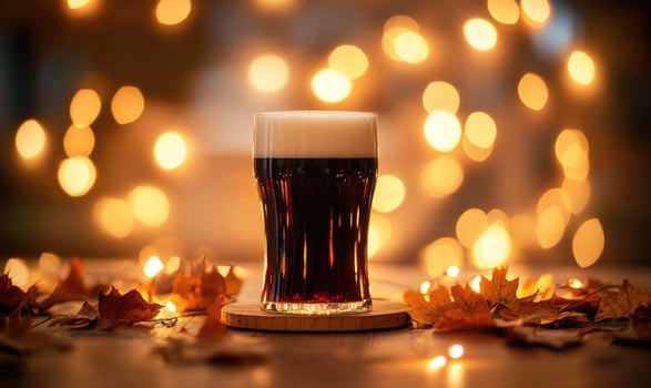 Pint of dark beer on wooden coaster, warm fairy lights, autumn leaves scattered photo