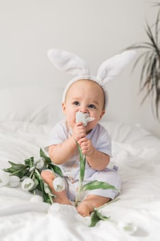 Cute funny baby with bunny ears, with a tulips at home on a bed of white bedding. Easter greeting card photo