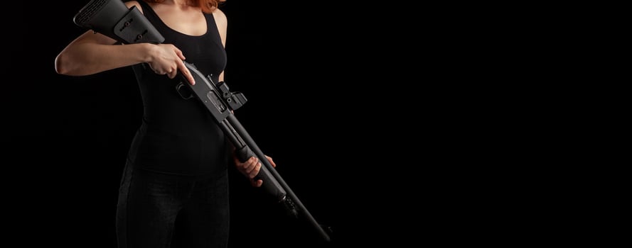 A girl in dark clothes on a black back holds a weapon in her hands. Concept for a poster about feminine power. photo