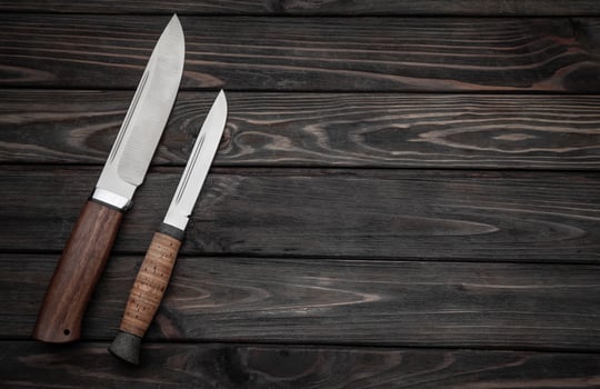 Hunting bowie knife with a wooden handle on dark wooden background. Steel arms weapon. top view photo